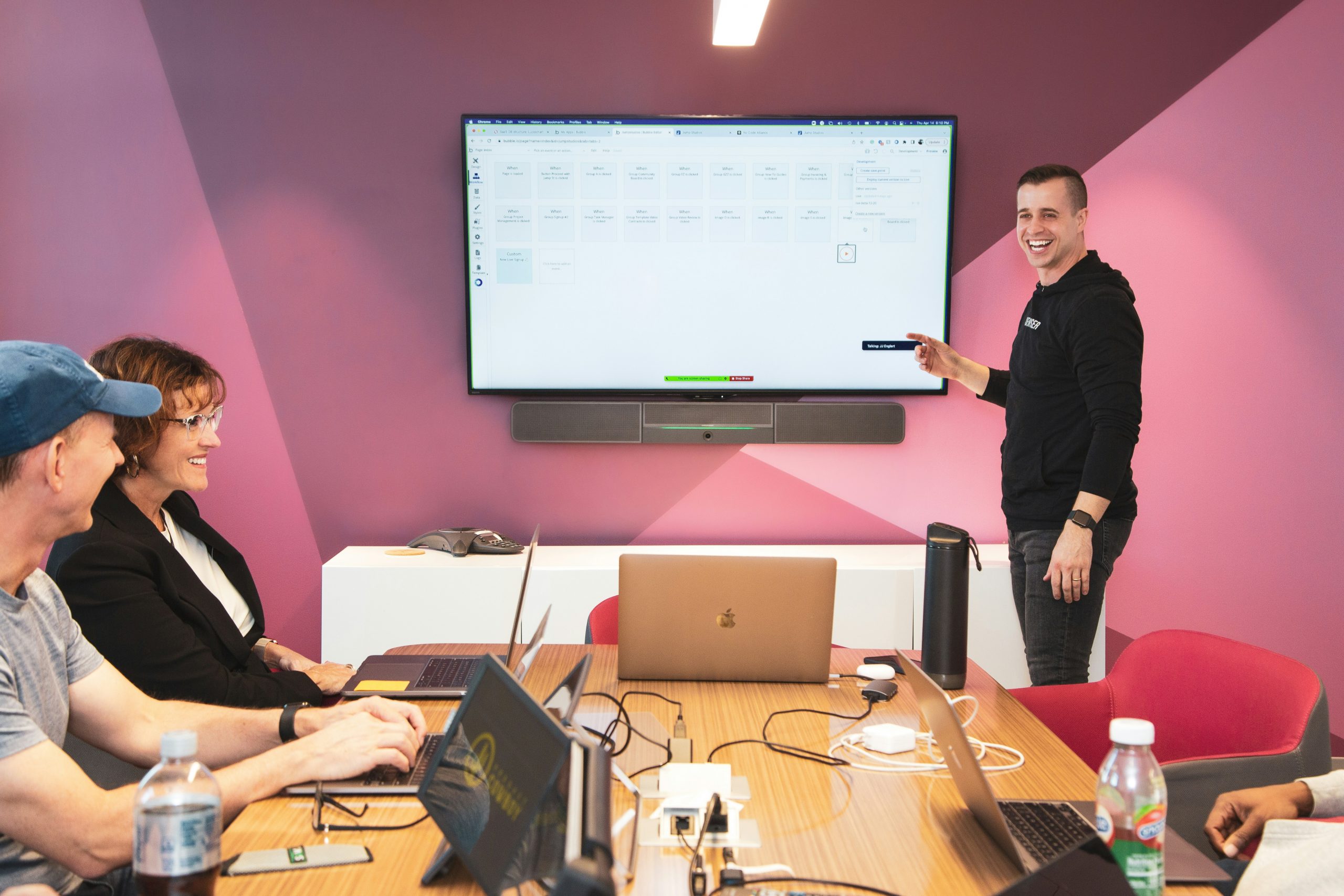 Team of enthusiastic professionals in a modern office looking at a large screen displaying complex data simplified into charts.