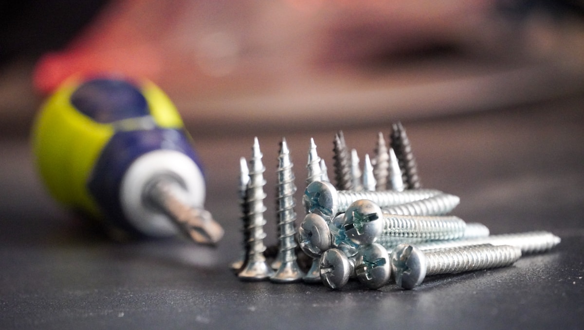 Vis à bois, tournevis et balle de tennis sur surface sombre.