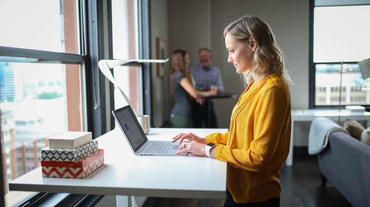 Femme blonde en vêtements jaunes travaillant sur un ordinateur portable dans un bureau.