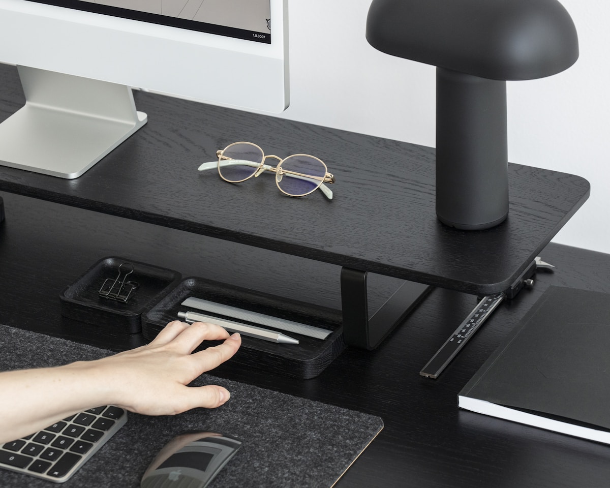 Bureau de travail moderne avec ordinateur, lampe et lunettes.