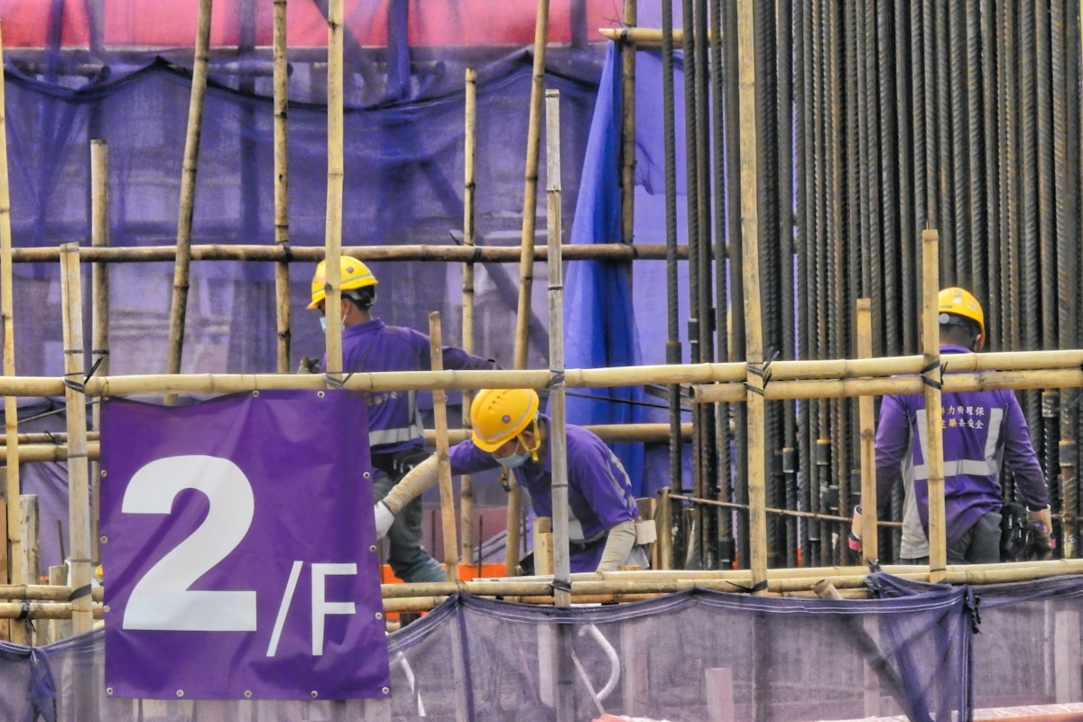 Échafaudage en bambou avec ouvriers en uniforme violet et casques jaunes.