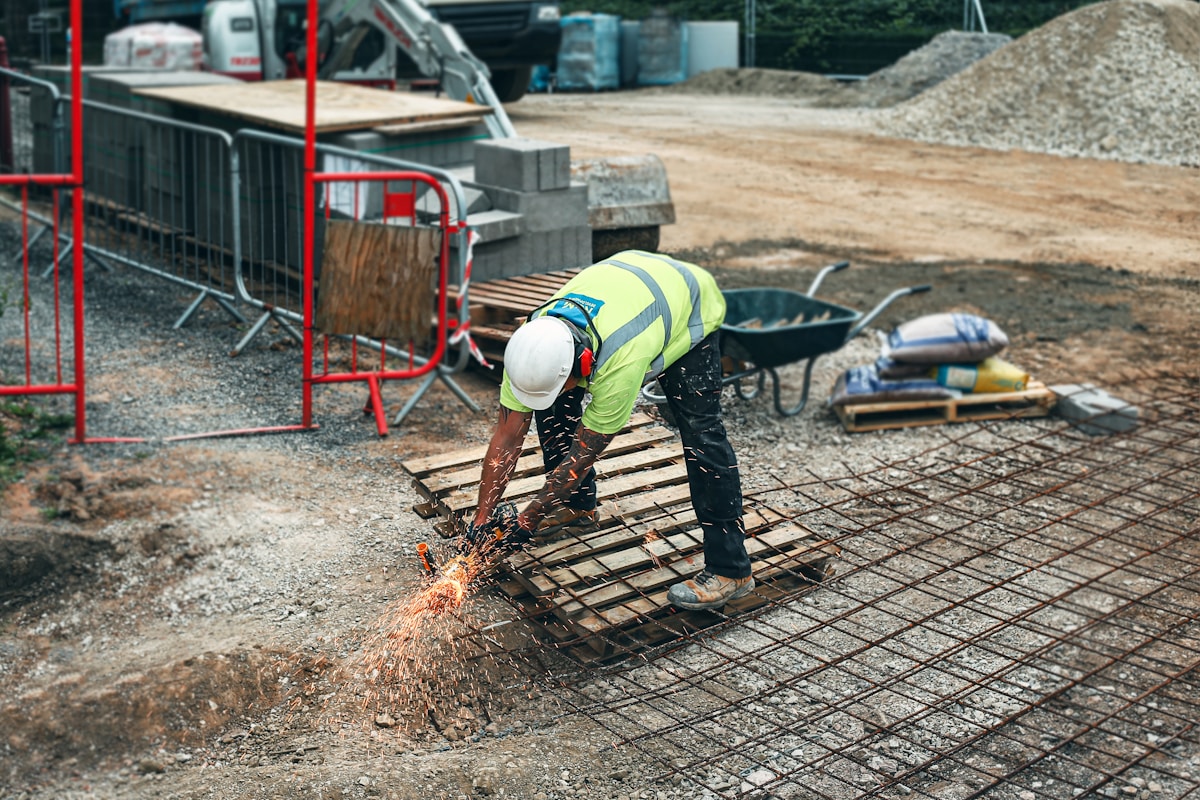Ouvrier en gilet de sécurité coupant du métal sur un chantier de construction.