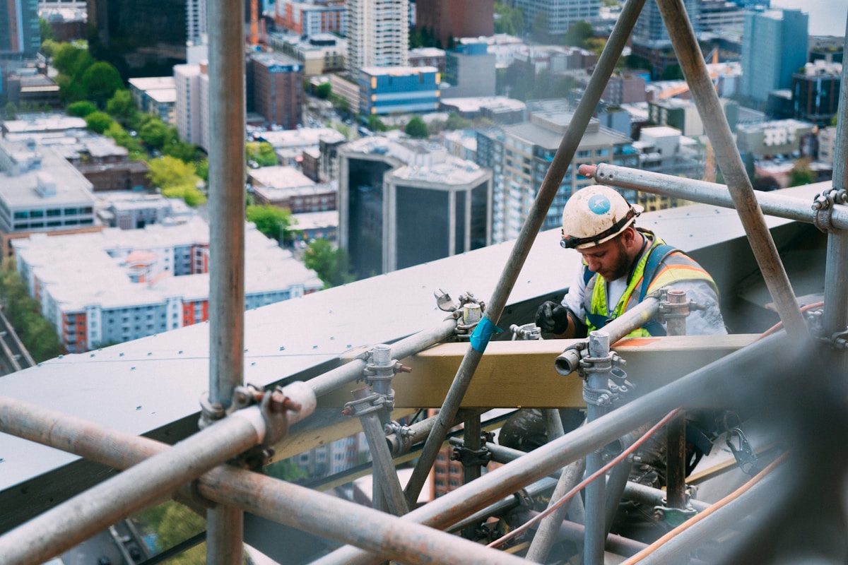 Ouvrier en harnais travaillant sur un échafaudage avec vue sur la ville.
