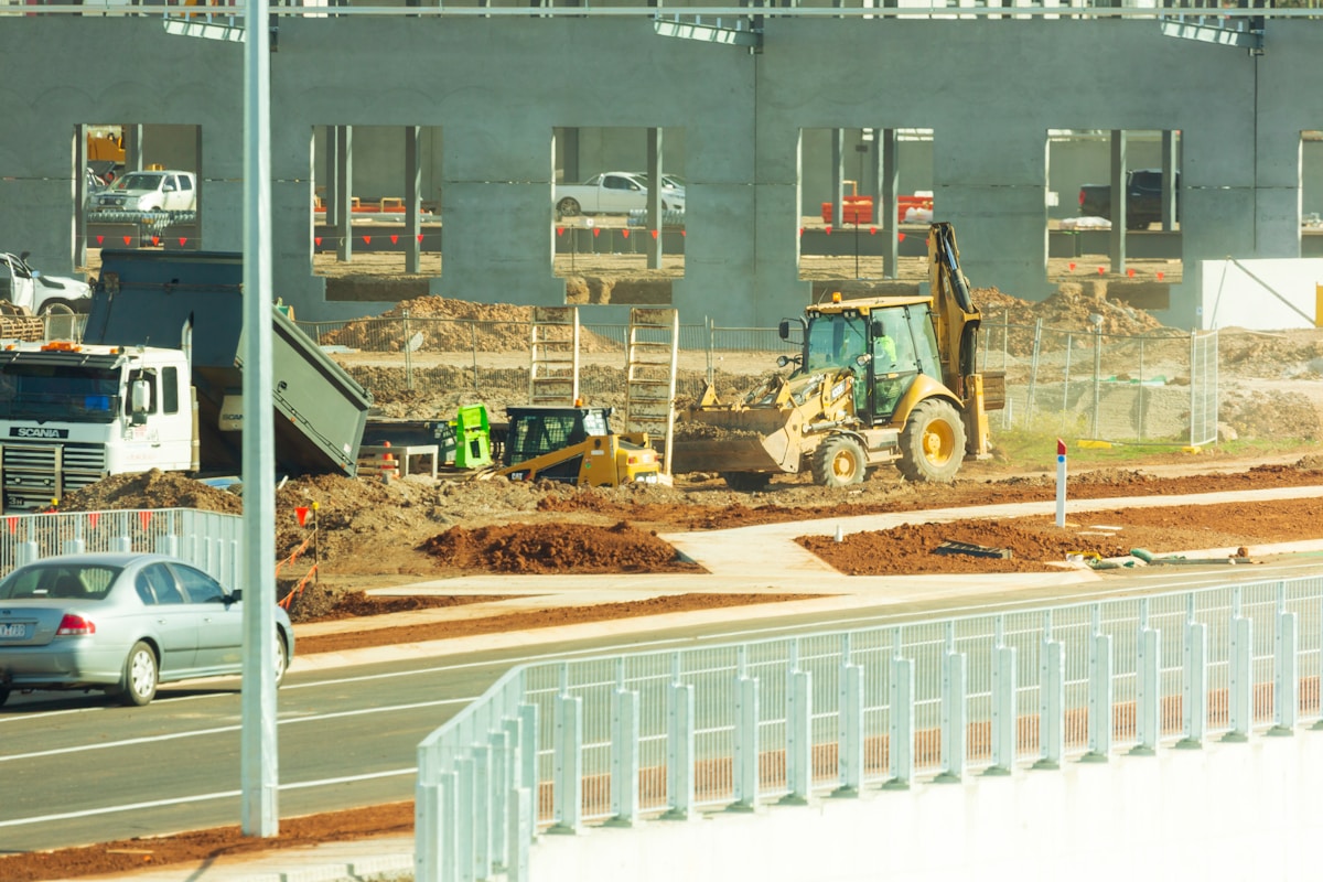 Chantier de construction avec pelleteuse, camions et matériaux.