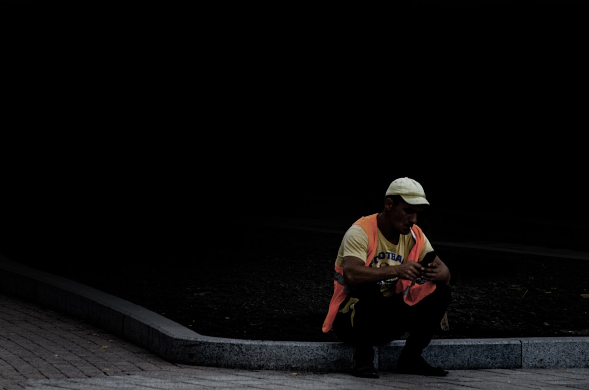 Homme assis sur un banc dans l'obscurité, vêtu d'un t-shirt rose.