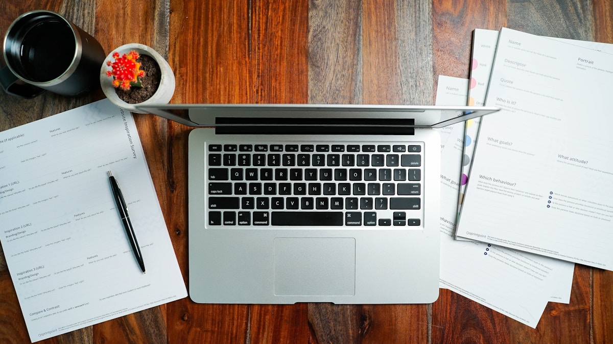 Bureau de travail avec ordinateur portable, documents et plante.